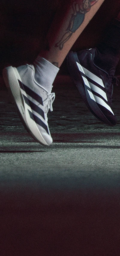 The image is an action photo showing a person running or training indoors. There are shoes against a black background. The shoes appear to be athletic footwear, possibly a model for advertisement given their placement in relation to the person's foot.