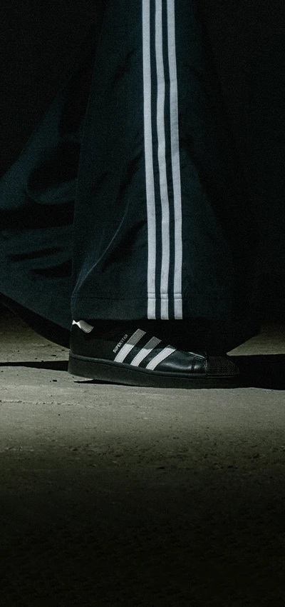 The image of a person standing and looking down, possibly at a sneaker. The person's identity is not being revealed here. In contrast, the image shows a sneaker prominently with what seems to be an advertisement or promotional material for it. 