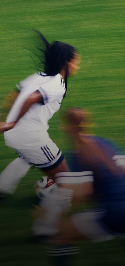 The image is a photo of a soccer player in action on the field. The player is blurred due to movement, indicating that they are running or have moved quickly during the moment captured.