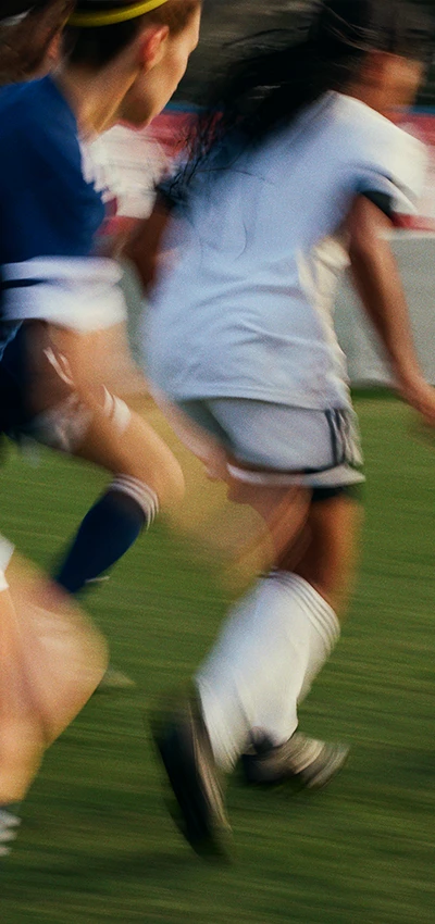 The image is a photo of a person running with other players in a sports field. The individuals are engaged in what looks like a soccer or futsal match.