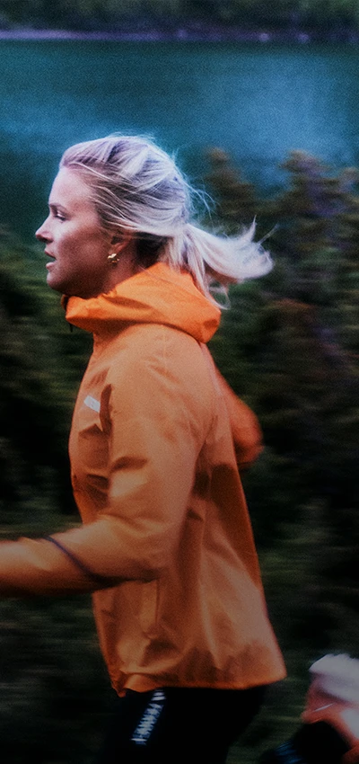 In the image, you can see a person running. The person is wearing an orange jacket and appears to be outdoors, as there's a green environment that suggests a forest or park setting.