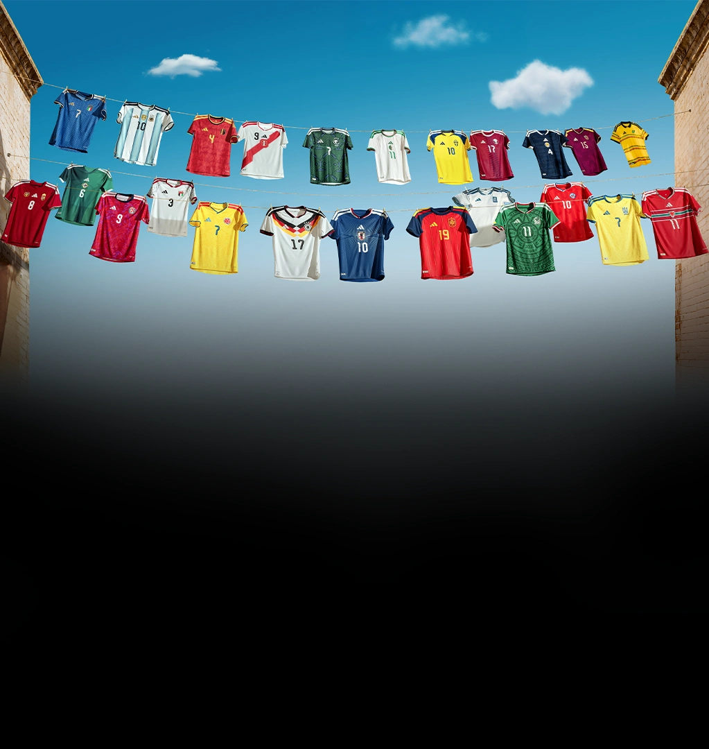 Mehrere internationale adidas Fußballtrikots hängen an Wäscheleinen zwischen zwei Gebäuden vor blauem Himmel. (Foto)