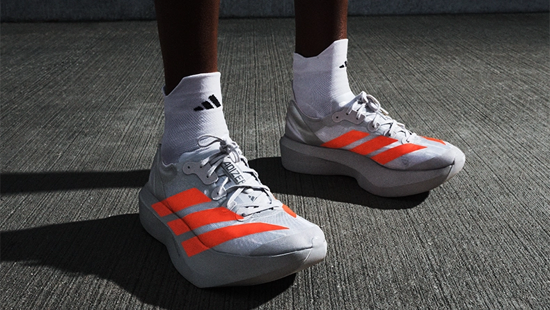 Person mit weißen Laufschuhen mit roten Streifen und weißen Socken, stehend auf Asphalt. (Foto)