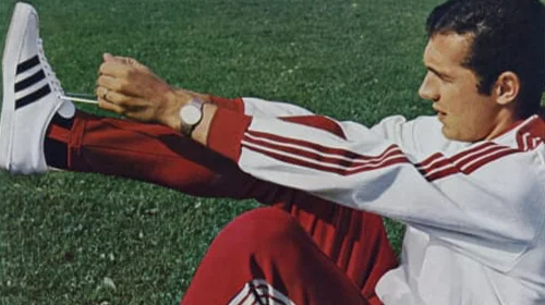 Mann im adidas Trainingsanzug beim Dehnen auf dem Spielfeld. (Foto)
