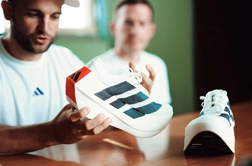 Zwei Männer betrachten und präsentieren einen adidas Laufschuh an einem Tisch. (Foto)