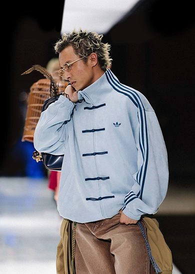 Model wearing a light blue adidas track top on a runway. (Photo)