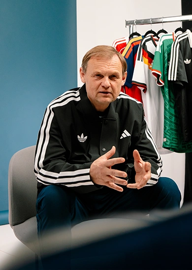 adidas CEO Bjørn Gulden wearing a black adidas jacket speaking in front of a rack of jerseys. (Photo)