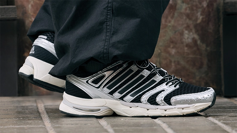 Close-up of black and silver sneakers worn by a person in loose black trousers, standing on a stone floor. (Photo)