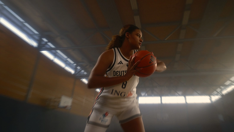 Woman in a white Germany basketball jersey holding a ball, moving inside a sports hall. (Photo)