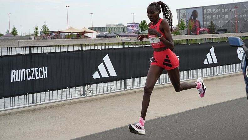 Woman in a red adidas running outfit racing along a road course past barriers with adidas logos. (Photo)